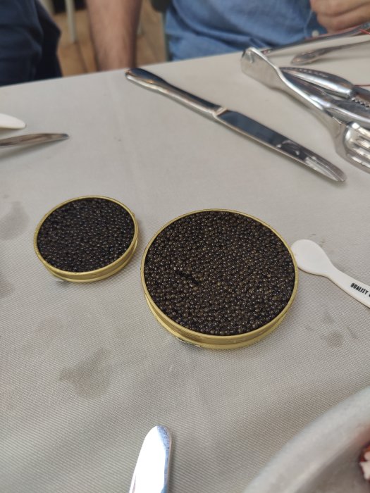 Två små burkar fyllda med svart kaviar på ett vitt dukat bord vid en tillställning.