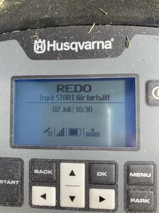 Display på en Husqvarna-automower visar redo-status, datum och tid samt ikoner för Bluetooth och GSM-signal.
