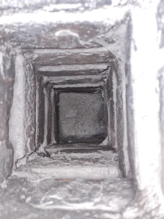 Vy neråt i en gammal rökkanal klädd med murbruk och sotiga kanter.