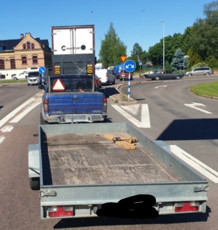 En hund ligger ovanpå en last på ett släp i trafik.