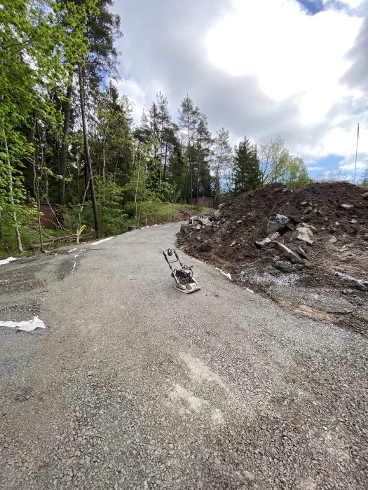 Nybyggd grusväg med padda för komprimering omgärdad av stora sten- och jordhögar på en byggarbetsplats.