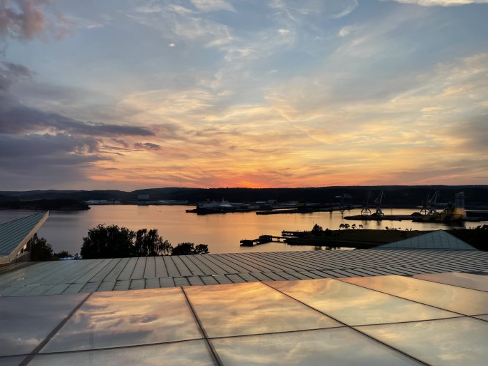 Kvällshimmel över hamn sett från ett hotelltak med reflekterande yta och solnedgång i bakgrunden.