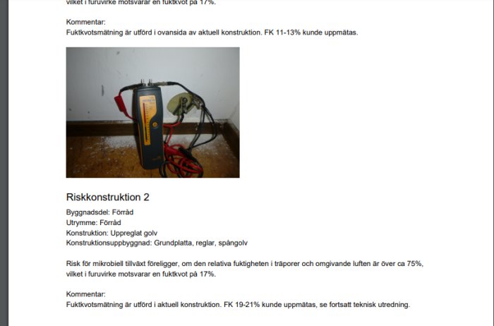 Fuktmätare med sladdar placerad på ett betonggolv i ett förråd med uppmätta fuktvärden.