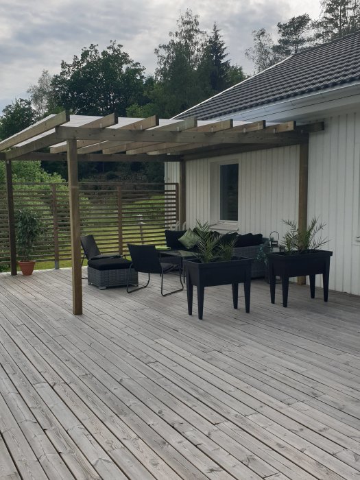 Nyligen färdigställd träpergola med tak över uteplats med trägolv, möbler och gröna växter.