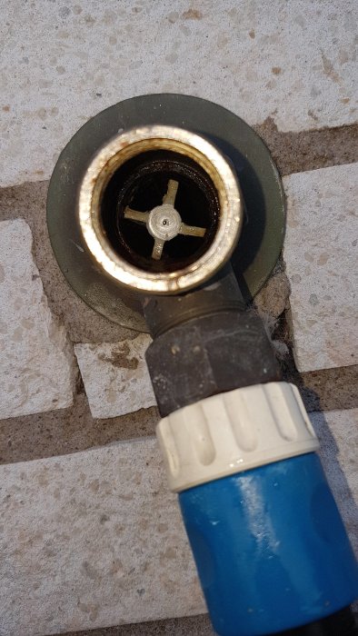 En bild av ett öppet avloppsrör med ett vitt kryss inuti och en blå slangenhet kopplad till röret.