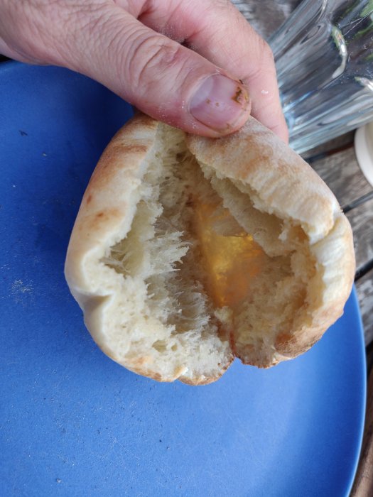 Nybakat pitabröd hållet i handen över en blå tallrik som visar den fluffiga insidan.