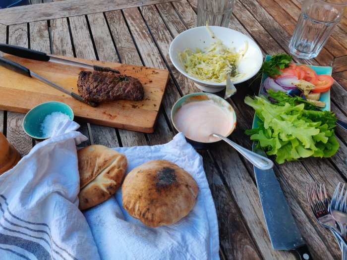 Hemgjorda pitabröd på träbord med grillad köttbit, sallad, sås och grönsaker.