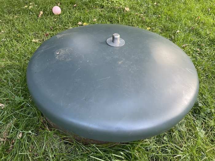 Plastbrunnslock på gräsmatta med en metallbult i mitten.