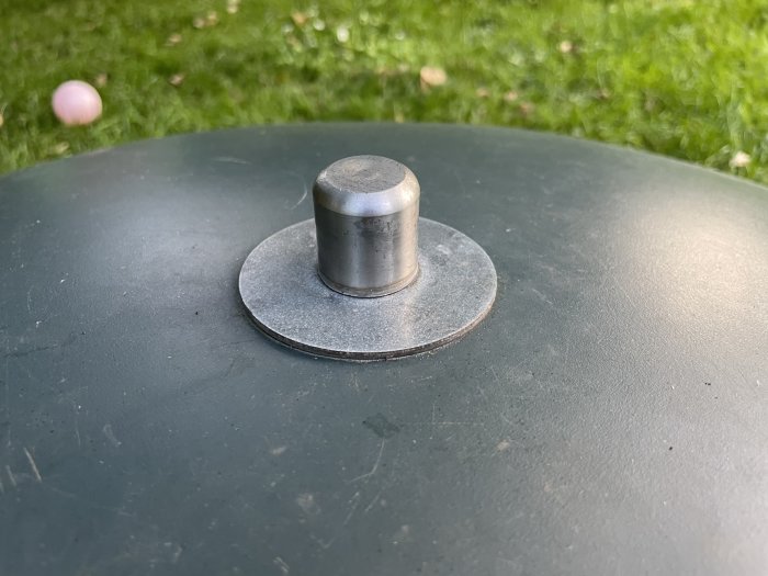 Plastbrunnslock med metallhandtag på gräsbackgrund.