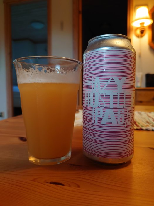 Ett glas öl bredvid en burk med texten "Hazy IPA" på ett träbord.