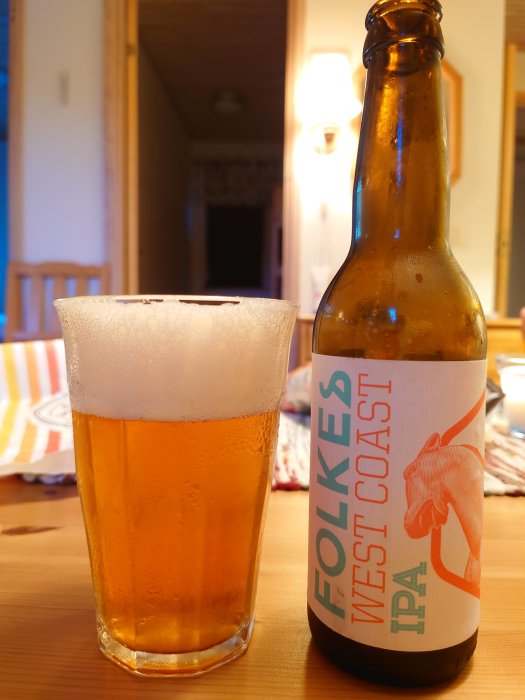 Ett glas öl och en flaska av Folkes West Coast IPA på ett bord.