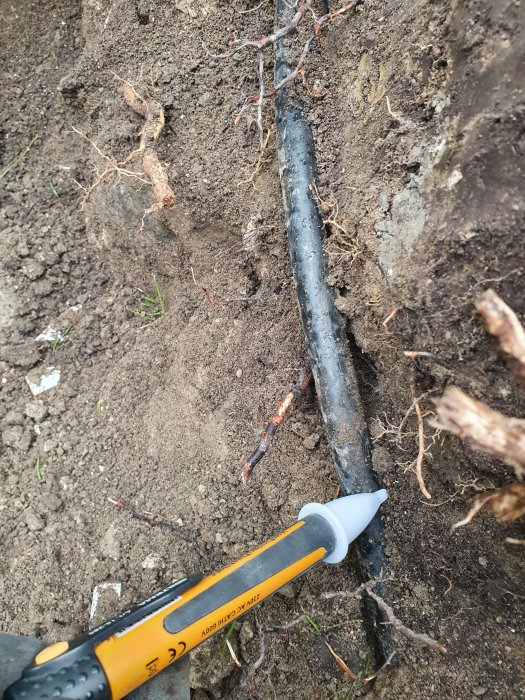 Nyupptäckt svart kraftkabel som är framgrävd på ca 30 cm djup med en spade nära, i jordig mark.