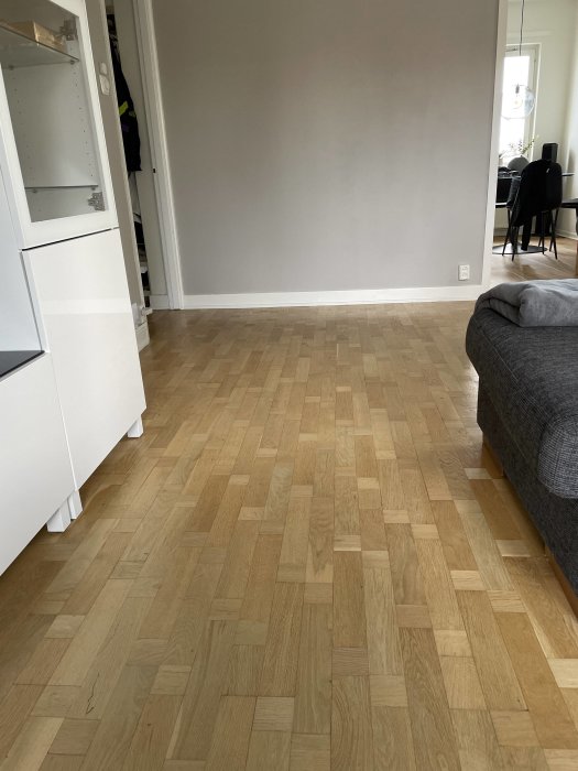 Trägolv med stavmönster i ett rum, vissa delar av golvet uppvisar skador från vattenincident.