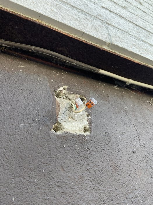 Eluttag halvt inmurat i en vägg med osläckt kabel och utsatt för väder och vind.