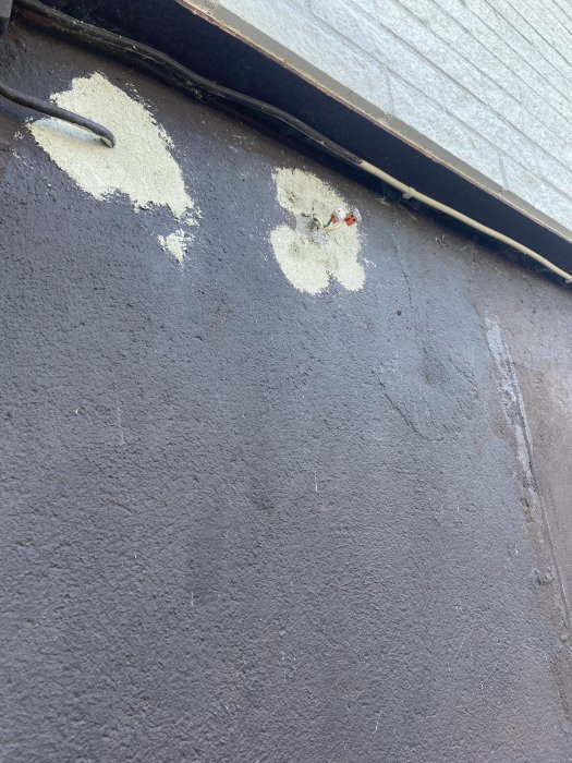 Mörk vägg med fläckar av avskalad färg och en synlig kabel löper längs med väggen.