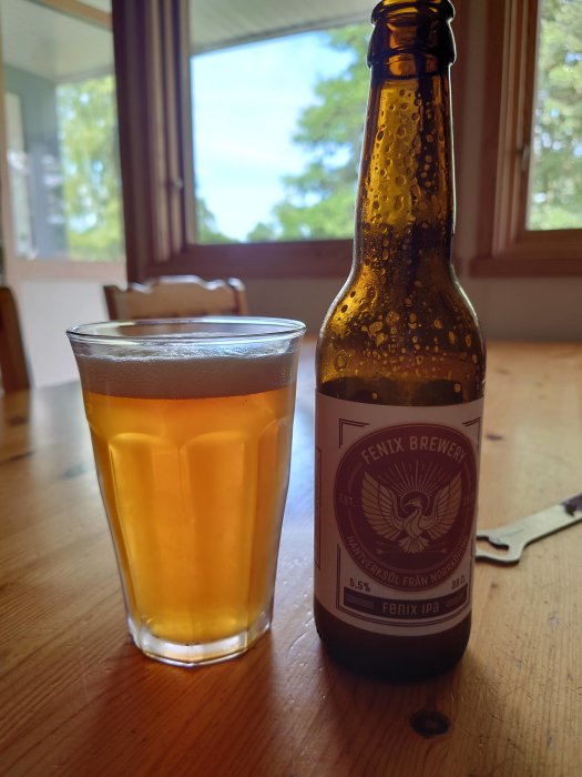 IPA-öl i glas bredvid en öppnad flaska från Fenix Brewery på ett träbord.