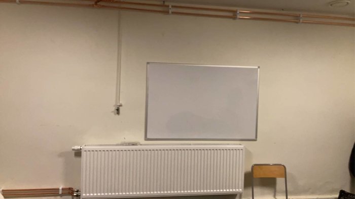 Tom vitmålad rumsvägg med whiteboard och element, redo för att inredas som ungdomsreplokal.