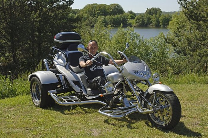 Man sitter på en silverfärgad trike nära en sjö på en solig dag.