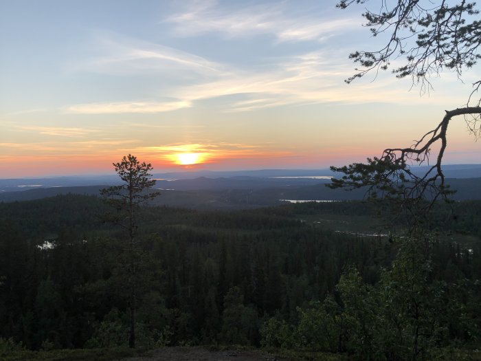 Solnedgång över skogsbeklädda kullar och sjöar sett från en utsiktsplats.