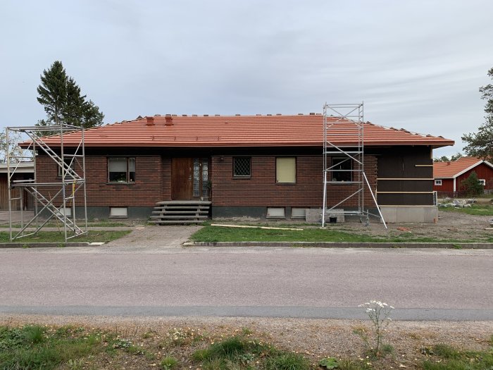 Tegelhus under renovering med nya röda betongpannor på taket, byggnadsställningar på sidan.