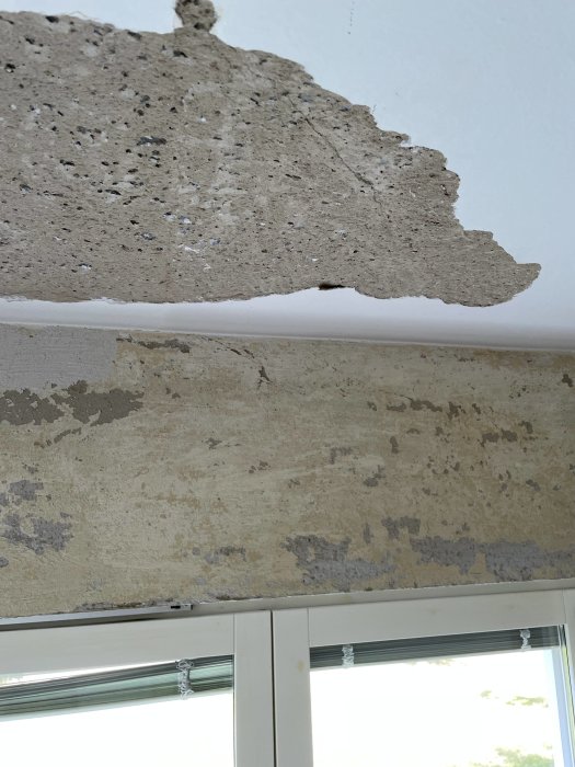 Skadat tak med bortskrapat lager visande poröst underlag vid ett fönster i en bostadsrätt från 50-talet.