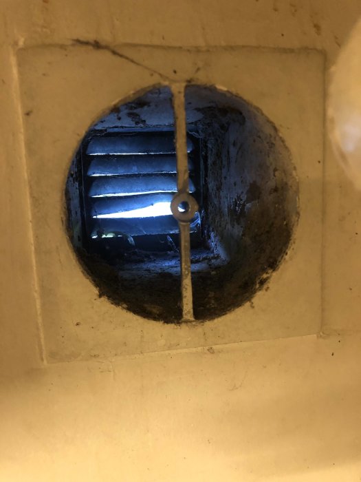 En enkel ventil i en betongvägg, synlig smuts och kondens, möjlig anslutning för köksfläkt i garagebyggprojekt.