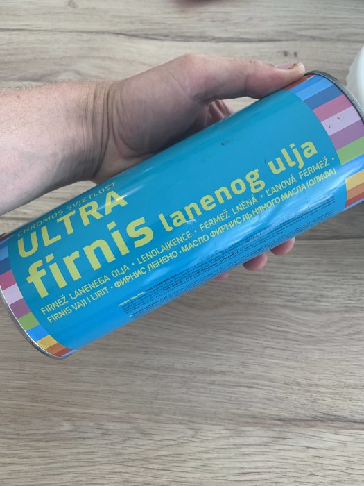 En hand håller en burk med text som antyder att det är linolja av okänd typ mot en träbakgrund.