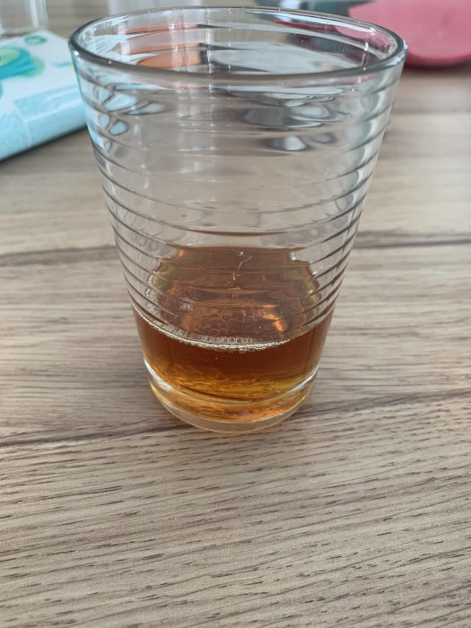 Ett glas med bärnstensfärgad vätska, möjlig linolja, på ett bord, osäkerhet om vätskan är rå eller kokt.