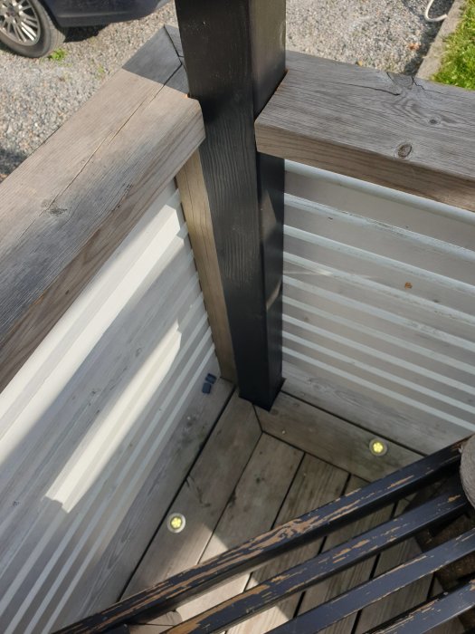 En pergolastolpe i svart som är monterad intill ett terrassräcke och skruvad i underliggande reglar.