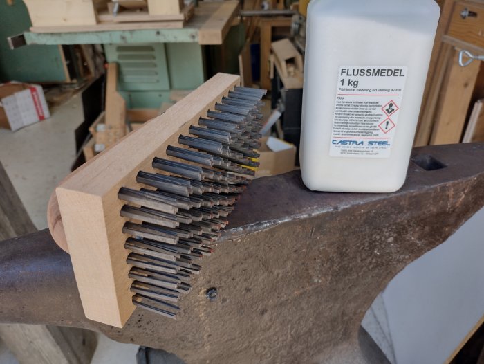 Smidesborste på en städ med en flaska flussmedel bredvid, verktyg för smide och vällning.