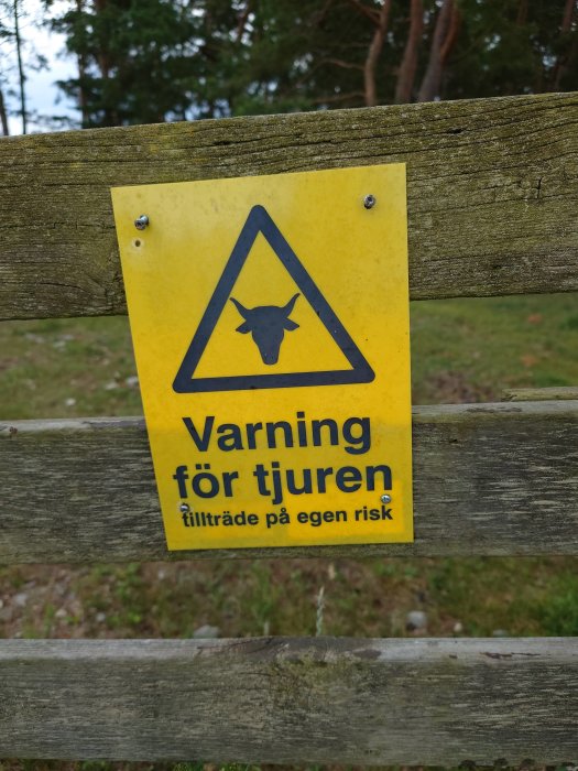 Varningsskylt på trästaket med texten "Varning för tjuren, tillträde på egen risk" och symbol för tjur.
