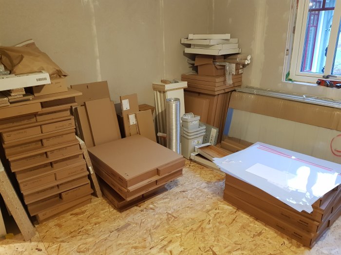 Nytt kök levererat i flera platta paket och byggmaterial staplade på golvet i ett rum under renovering.