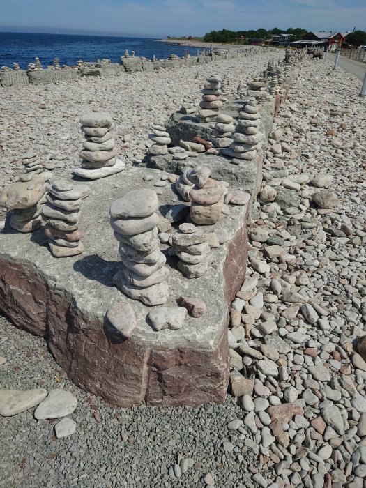 Stenpelare staplade i olika höjder på en kust med klappersten och havet i bakgrunden.