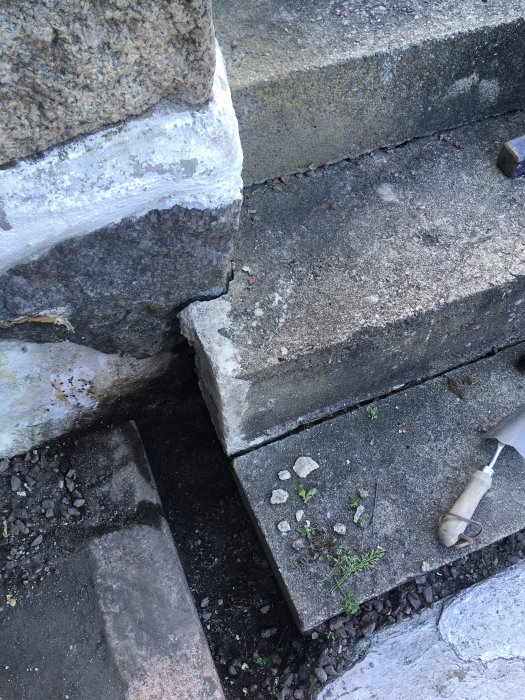 Sprucket hörn på betongtrapp där tegelsten och betong separerat och ett verktyg syns.