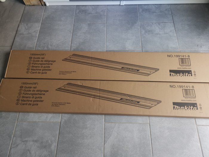 Två långa kartonger märkta Makita för skensystem på ett grått klinkergolv.