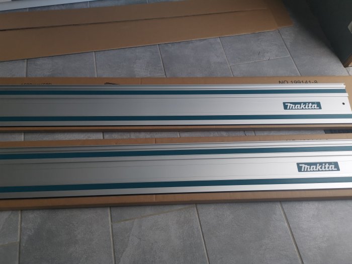 Två nya Makita guider för sågning utpackade och placerade på ett golv med gråa kakelplattor.