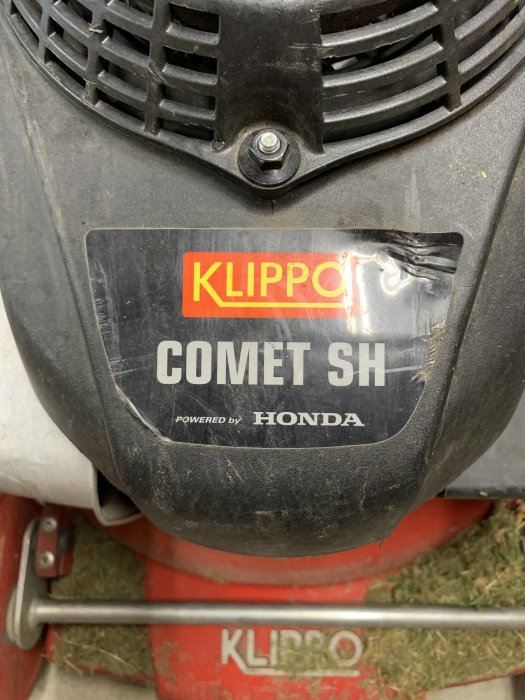 Skadad Klippo Comet SH gräsklippare med Honda-motor, där klistermärket är trasigt och tecken på användning syns.