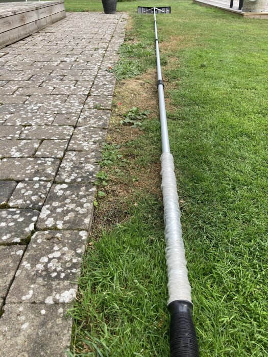 En fem meter lång snöraka utsträckt på marken bredvid stenplattor och gräs.