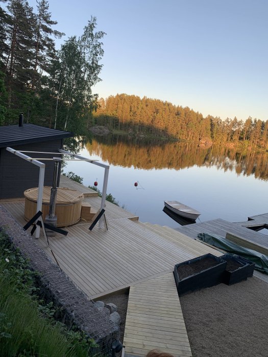 Nybyggd träaltan vid sjö med bastu och båt i mjuk kvällsbelysning.