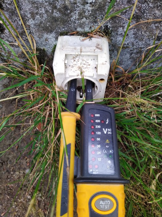 Multimeter testar spänning på en väderexponerad utomhus strömbrytare mot bakgrund av gräs.