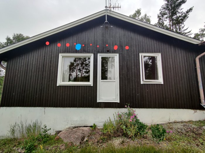 Husfasad med markerade spikar i rött och planerat ventilationshål i blått ovanför två fönster.
