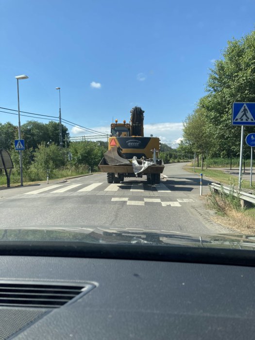 Utsikt från en bil framåt mot en fartgupp där en padda studsar bakom en lastbil på en solig dag.