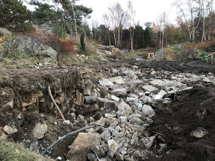 Byggarbetsplats med nedrivna grundrester och utspridda stenblock på jordig mark.