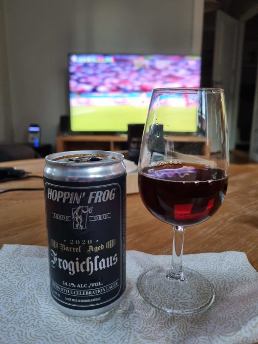 Ölburk och glas på bord med fotbollsmatch på TV i bakgrunden.