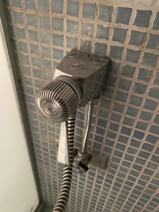 Läckande engreppsblandare monterad på kakelvägg i dusch med blått mosaikmönster.