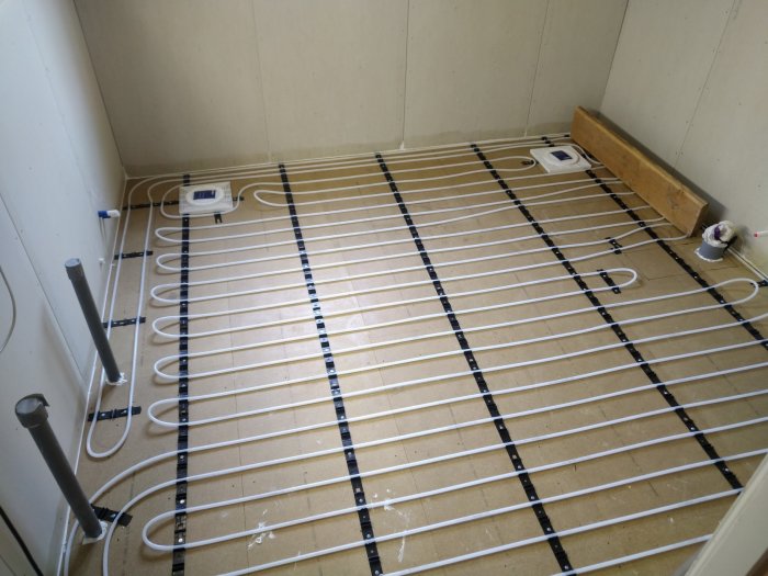 Installation av golvvärme med vita rör fästa på isolerplattor på ett oavslutat golv.