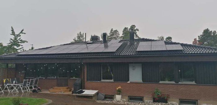 Ett enplans elementhus från 1975 med solpaneler på taket och en uteplats med trädgårdsmöbler.