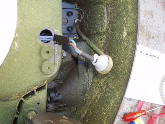 Öppen komponent av en Husqvarna Automower 330x med synliga kablar och delar, samt verktyg och gräsrester.