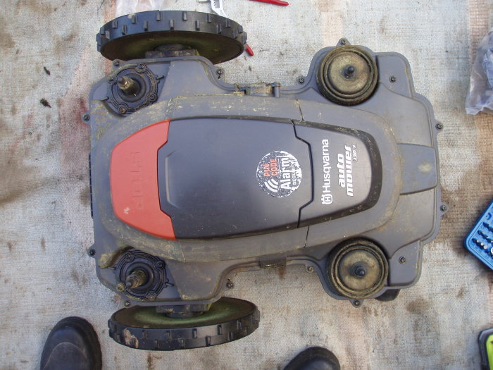 Undersidan av en Husqvarna Automower 330x på marken med synliga hjul och klippenhet.
