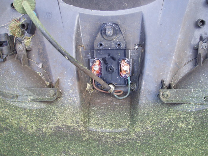 Undersidan av en Husqvarna Automower 330x med gamla, öppnade och ärgade batterier synliga och gräsrester.